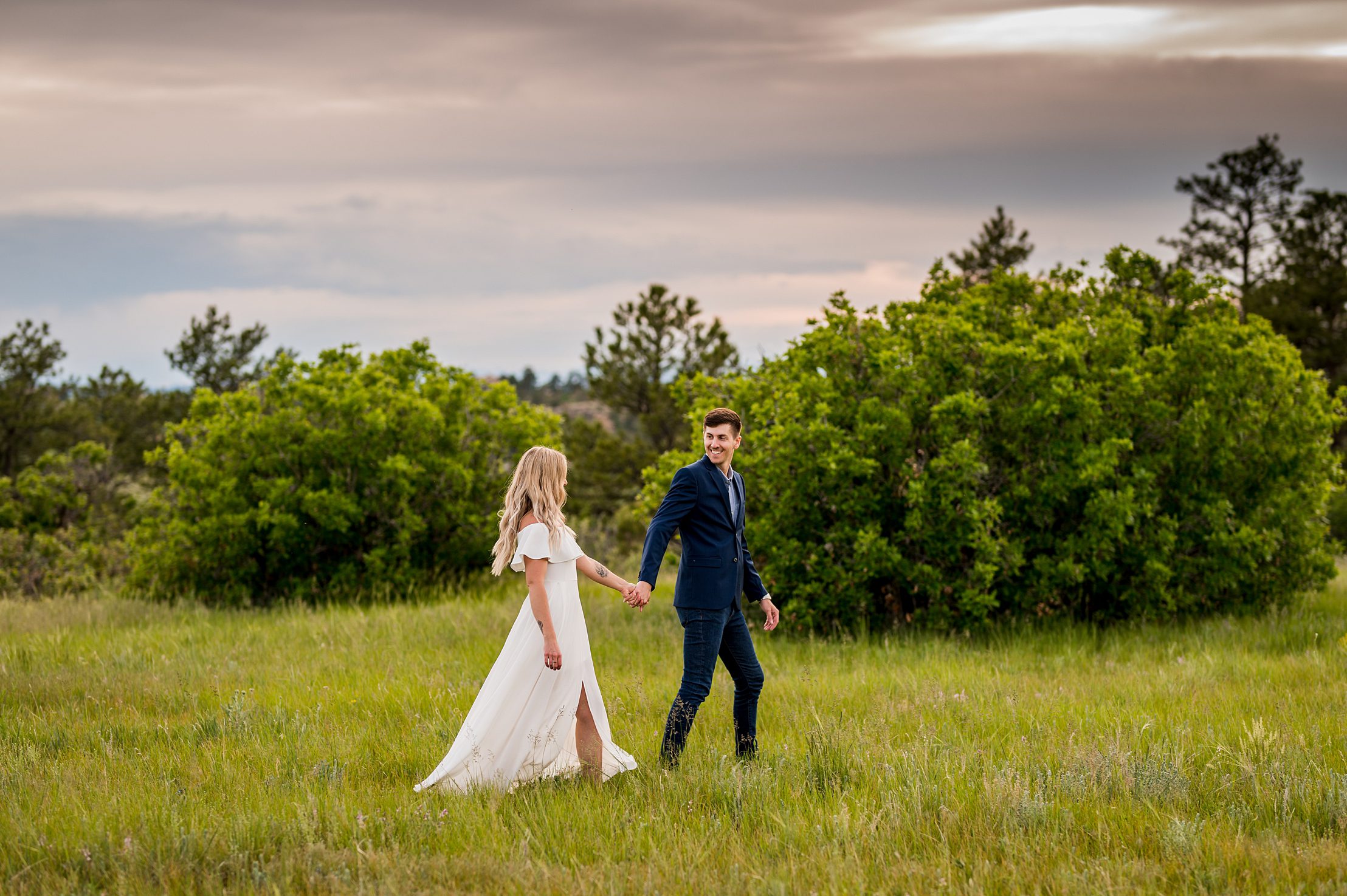 engaged couple walking through a green field with the sunset