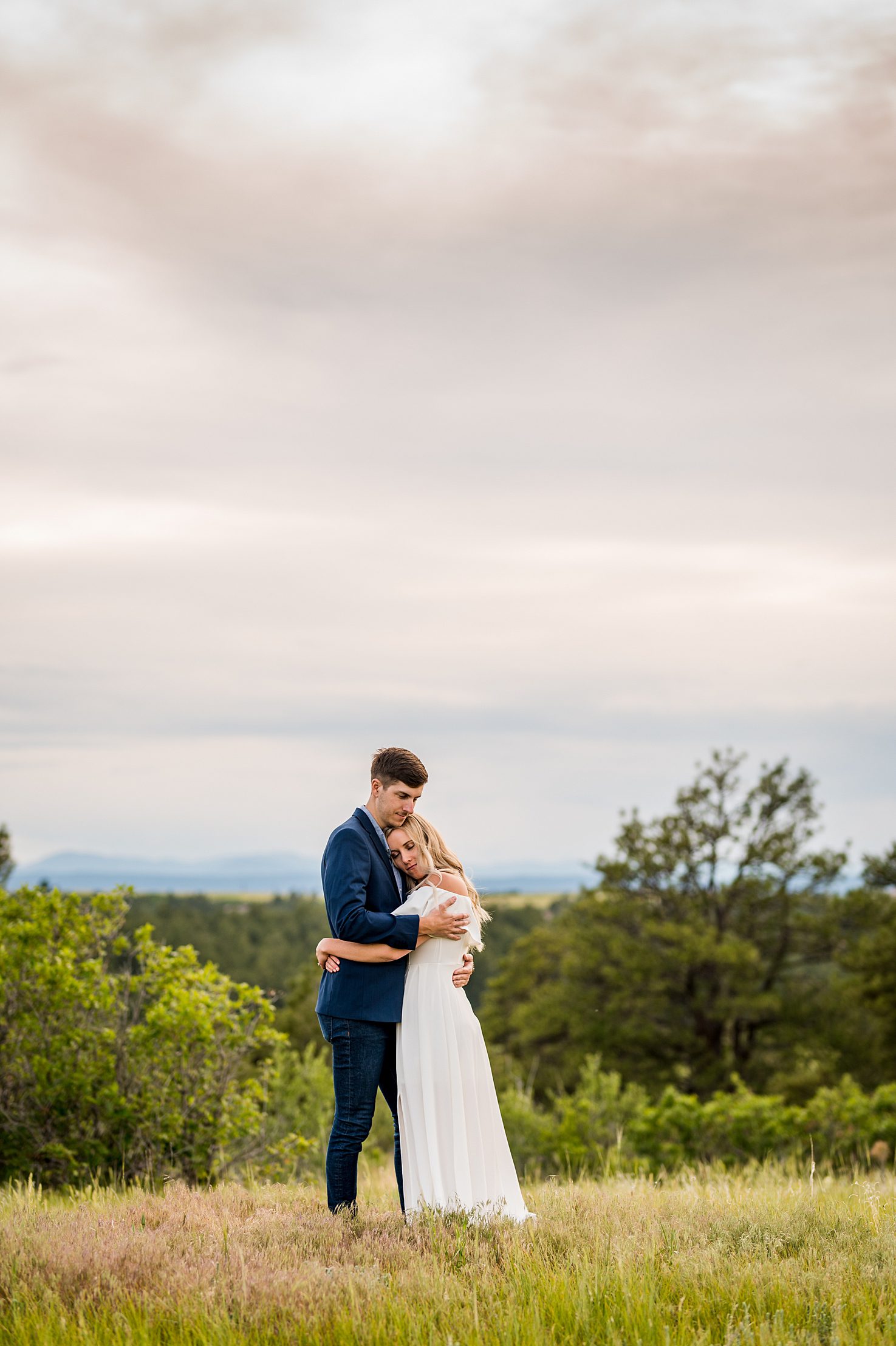 groom to be holding his fiancé in a field with the sunset behind them