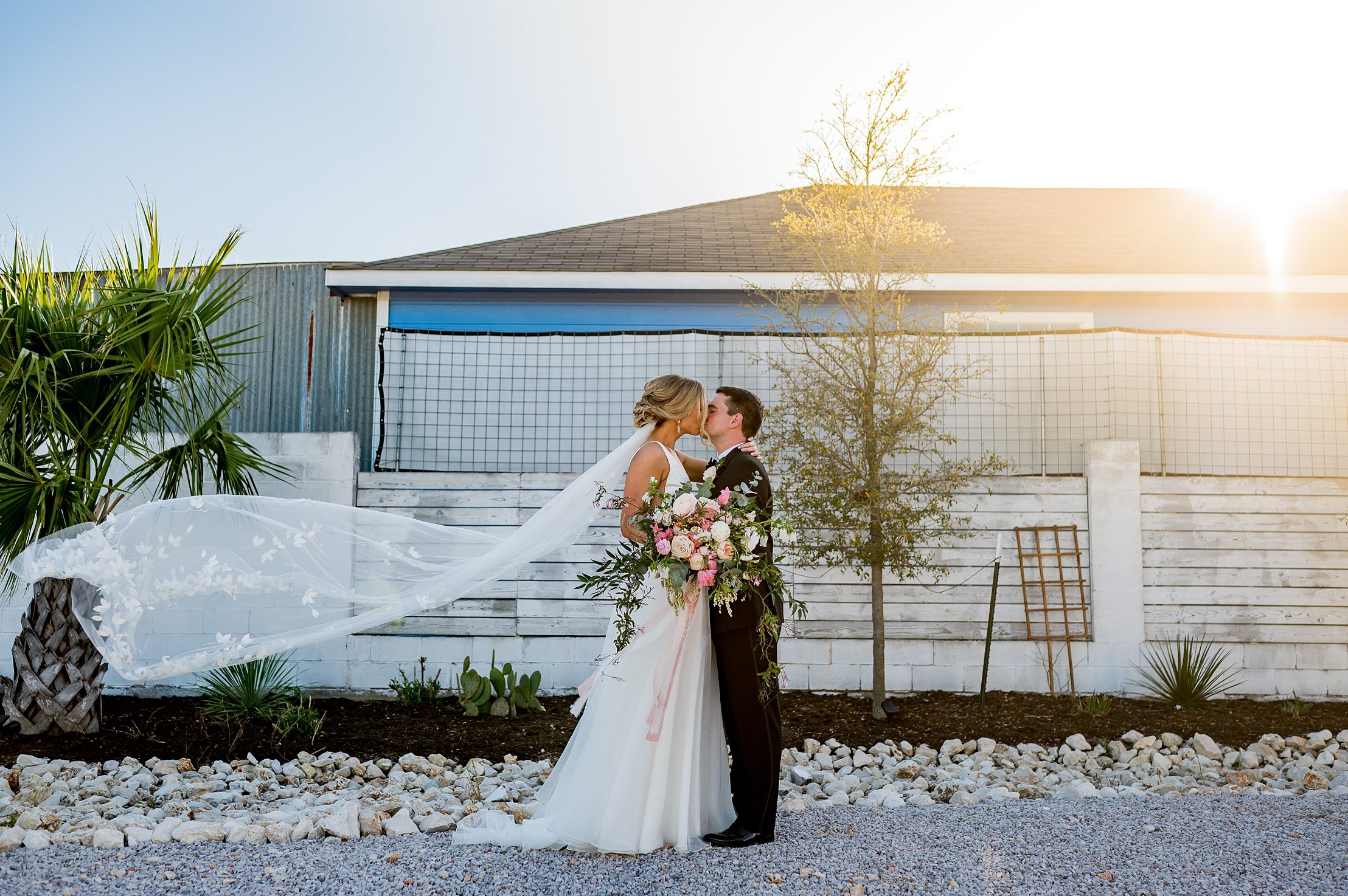 brides veil blowing in the wind while they kiss at a Texas wedding venue