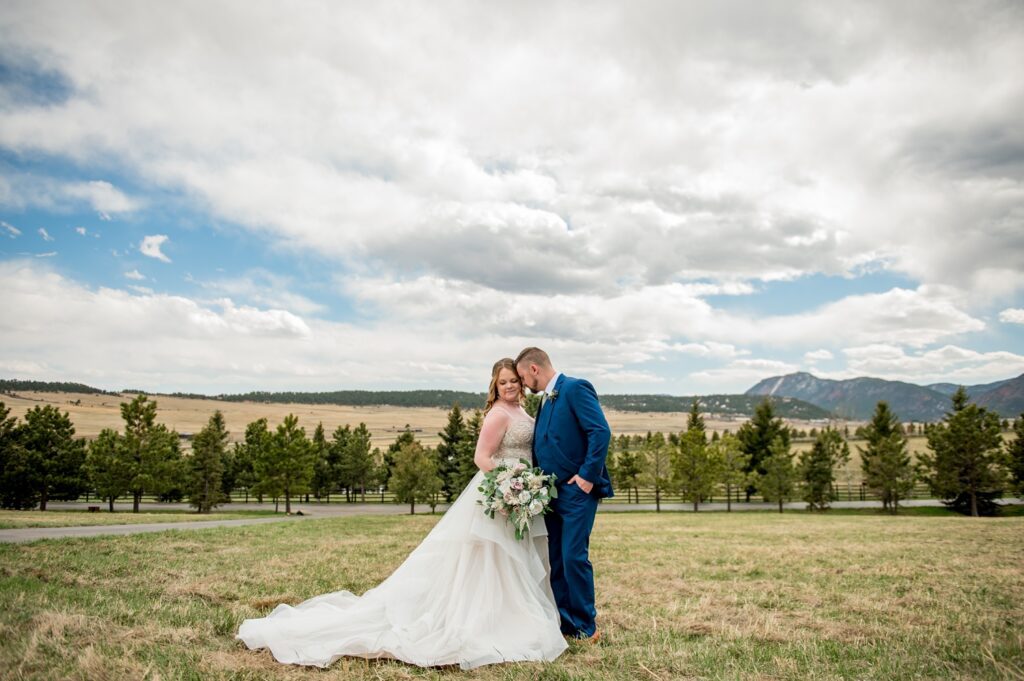 The bride and groom enjoy a quiet, intimate moment alone during their wedding portraits, embracing each other in a serene setting at Spruce Mountain Ranch. The couple shares a tender gaze, with the natural beauty of the Colorado landscape surrounding them, capturing the essence of their love and connection.