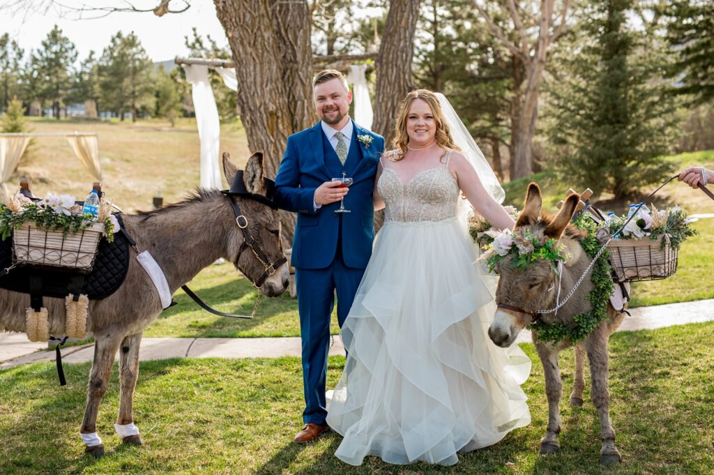 The bride and groom enjoy a fun moment during cocktail hour, sipping drinks while playfully interacting with beverage donkeys at their wedding. The adorable donkeys, adorned with decorative saddlebags, add a whimsical and unique touch to the celebration, creating a memorable experience for the couple and their guests.