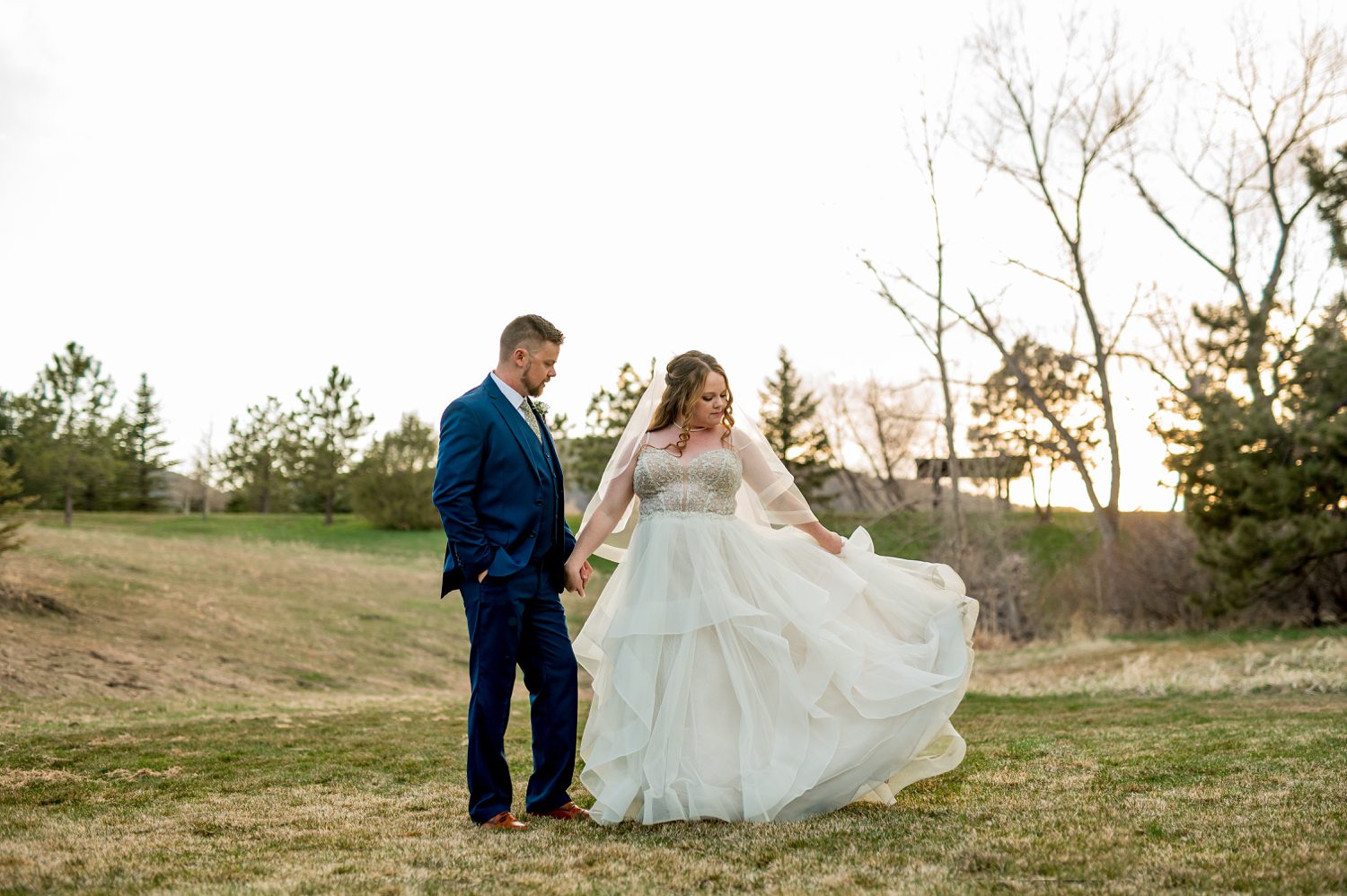 A bride and groom share an intimate moment during sunset at Spruce Mountain Ranch, silhouetted against a warm, glowing sky with the rugged Colorado mountains in the background, surrounded by soft golden light that enhances the romantic atmosphere.