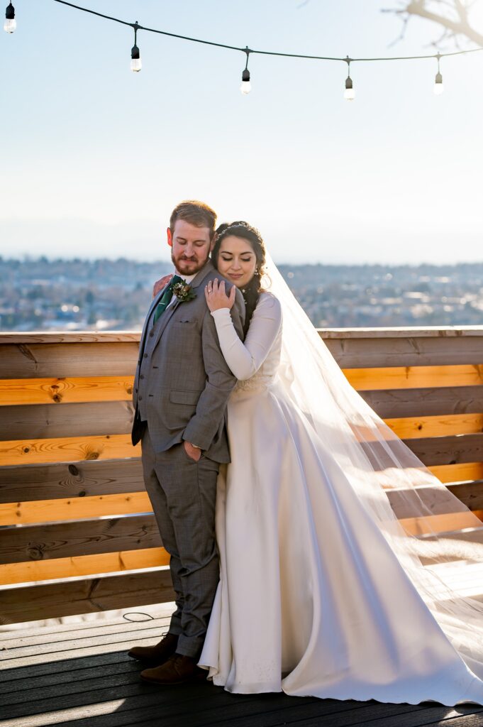 A bride and groom stand together at a beautiful Colorado wedding venue, surrounded by stunning mountain views and lush greenery. The couple shares a moment of joy, with the bride in her elegant gown and the groom in a sharp suit, capturing the love and beauty of their special day.