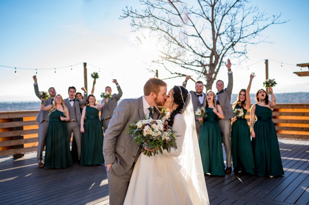 Bride and groom kiss as the bridal party cheers in the background in Colorado.