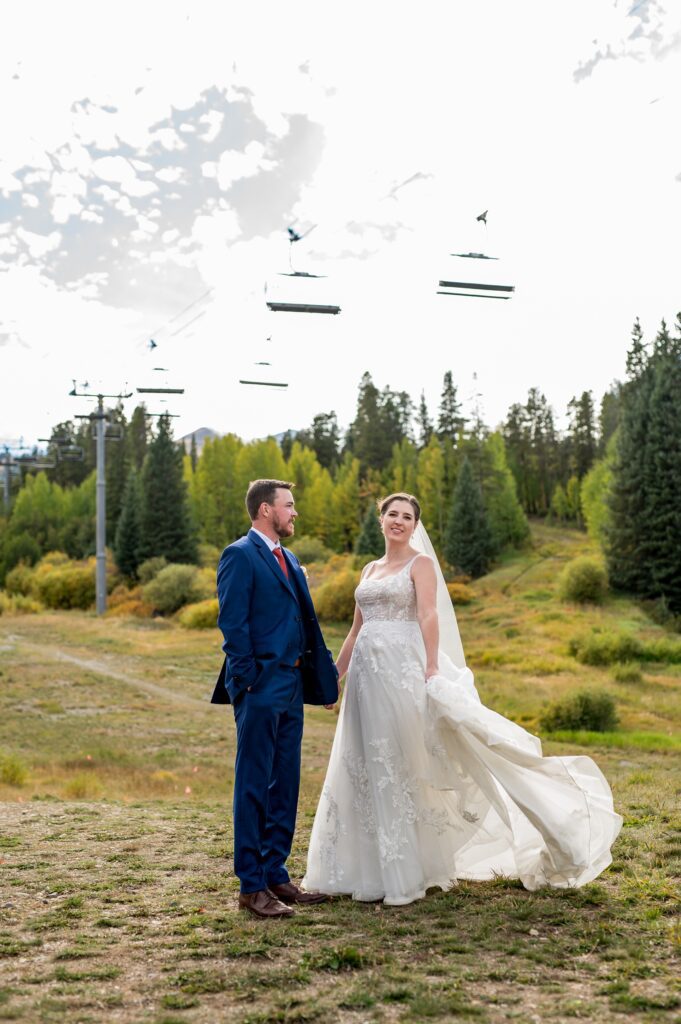 Bride and groom tie the knot at a Colorado mountain wedding venue nestled under the ski lifts with amber fall leaves framing them. The bride's long dress flits about as they share a happy time, frozen in time by a Colorado wedding photographer.