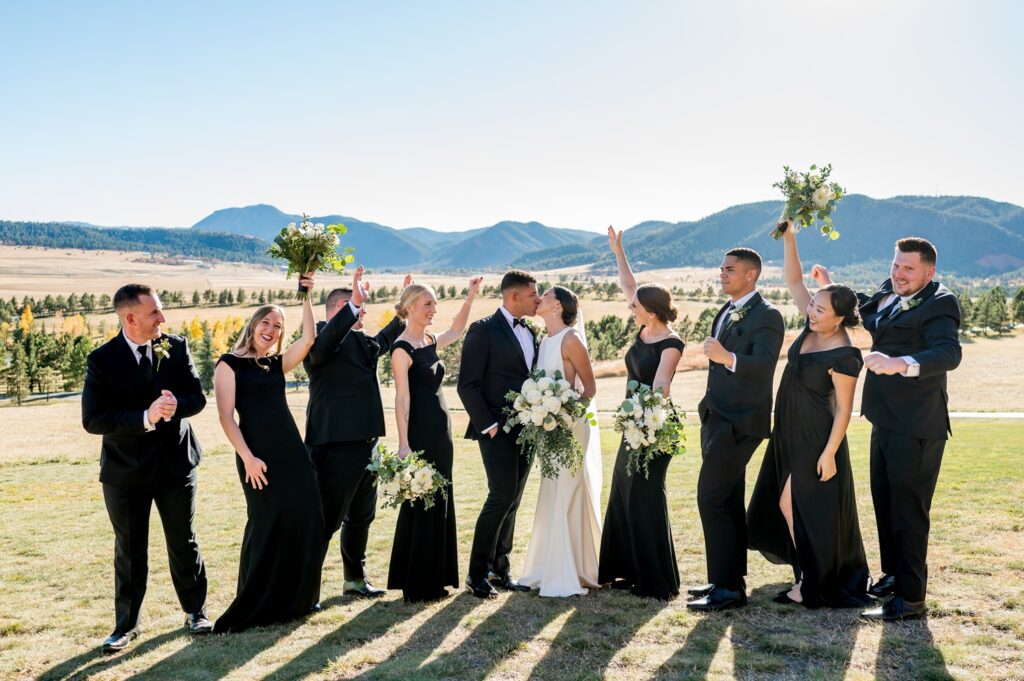 Bride and groom celebrate with their wedding party against the stunning mountain backdrop at Spruce Mountain Ranch in Colorado. True-to-color wedding photography capturing a joyful moment at a top Colorado wedding venue.