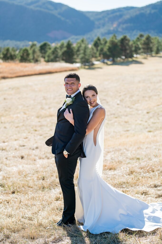 Bride and groom in a meadow filled with sunlight amidst the staggering mountain backdrop at Spruce Mountain Ranch, Colorado. This is true-to-color wedding photography of romance on an elegant fall wedding at one of Colorado's premiere wedding venues
