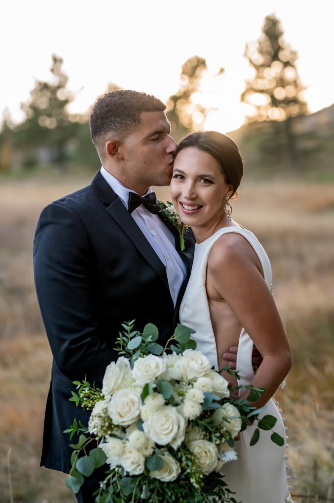 groom kisses his bride on the head during beautiful golden light at Spruce mountain ranch in Colorado