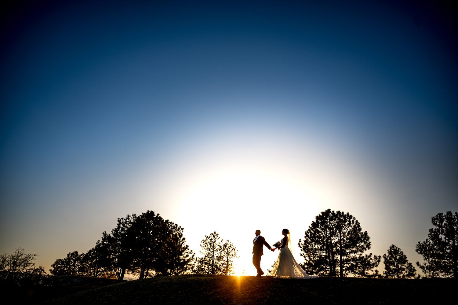Silhouetted bride and groom holding hands at sunset during a winter wedding at Sanctuary Golf Course in Colorado, photographed by a Colorado wedding photographer.